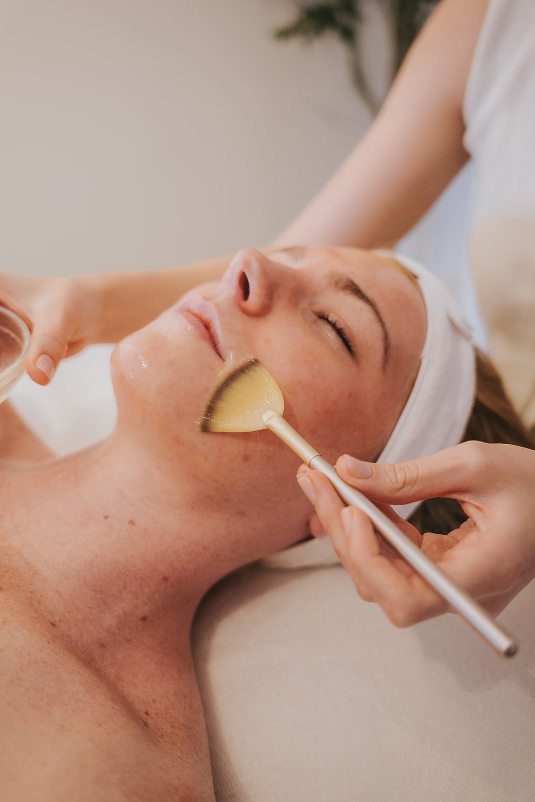 A person enjoys a luxurious facial treatment, lying peacefully with eyes closed and a white headband in place.