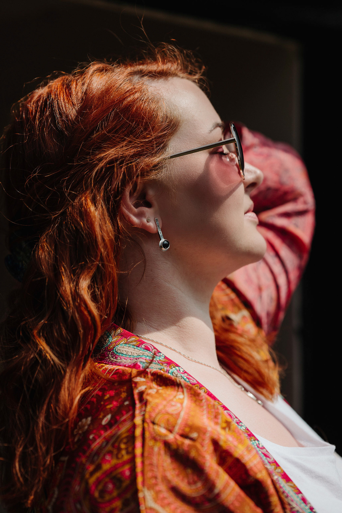 In a striking display of personal branding, a woman with long red hair and sunglasses dons a colourful paisley kimono over a white top.