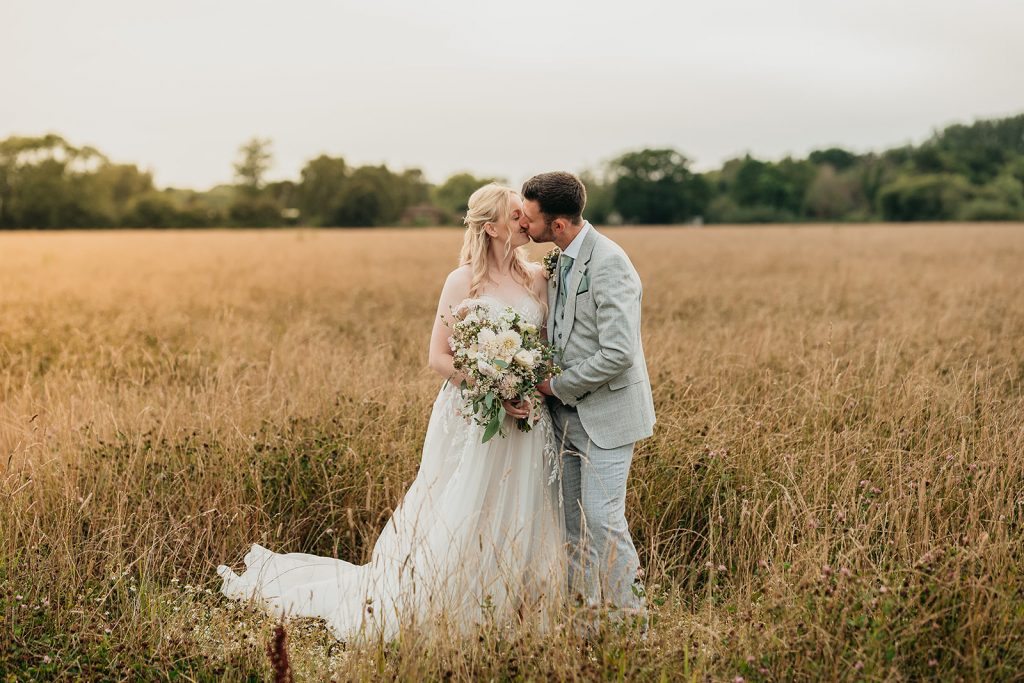 A bride and groom kiss in a grassy field West Sussex wedding at Southend Barns, Chicester.