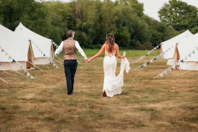 Two Woods Estate couple walk with backs to us, with bell tents to the side.