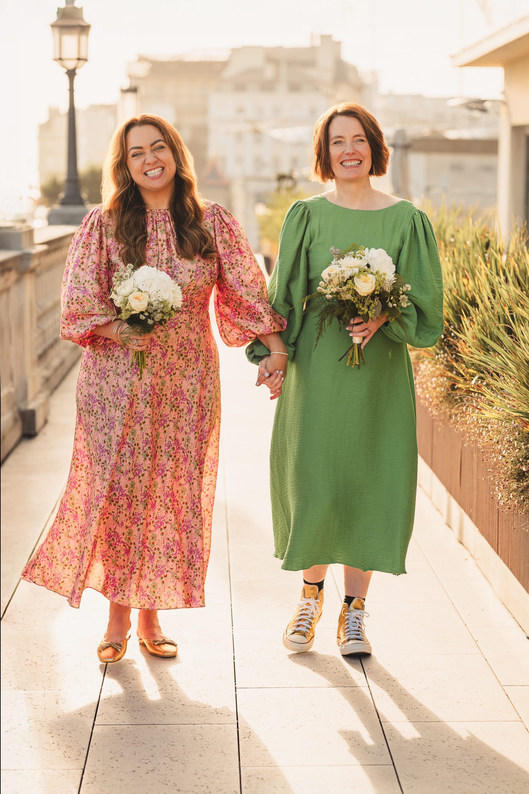 Two brides in green and pink outfits walking hand in hand on a Brighton rooftop terrace after their Brighton Town Hall wedding
