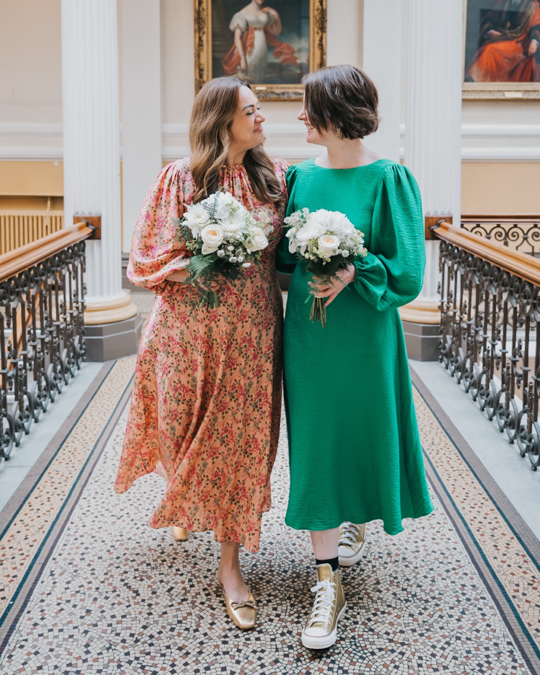 Two brides in green and pink outfits on the historic staircase at Brighton Town Hall