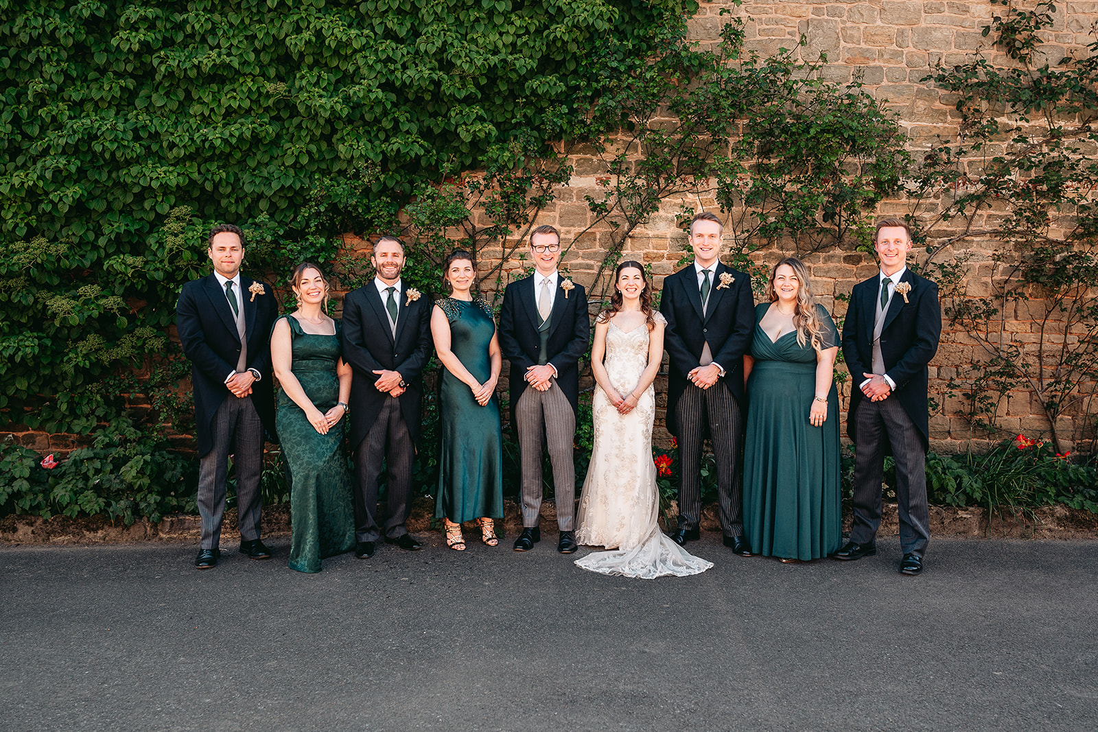 A relaxed wedding party group photograph beside the stone walls at Fitzleroi Barn